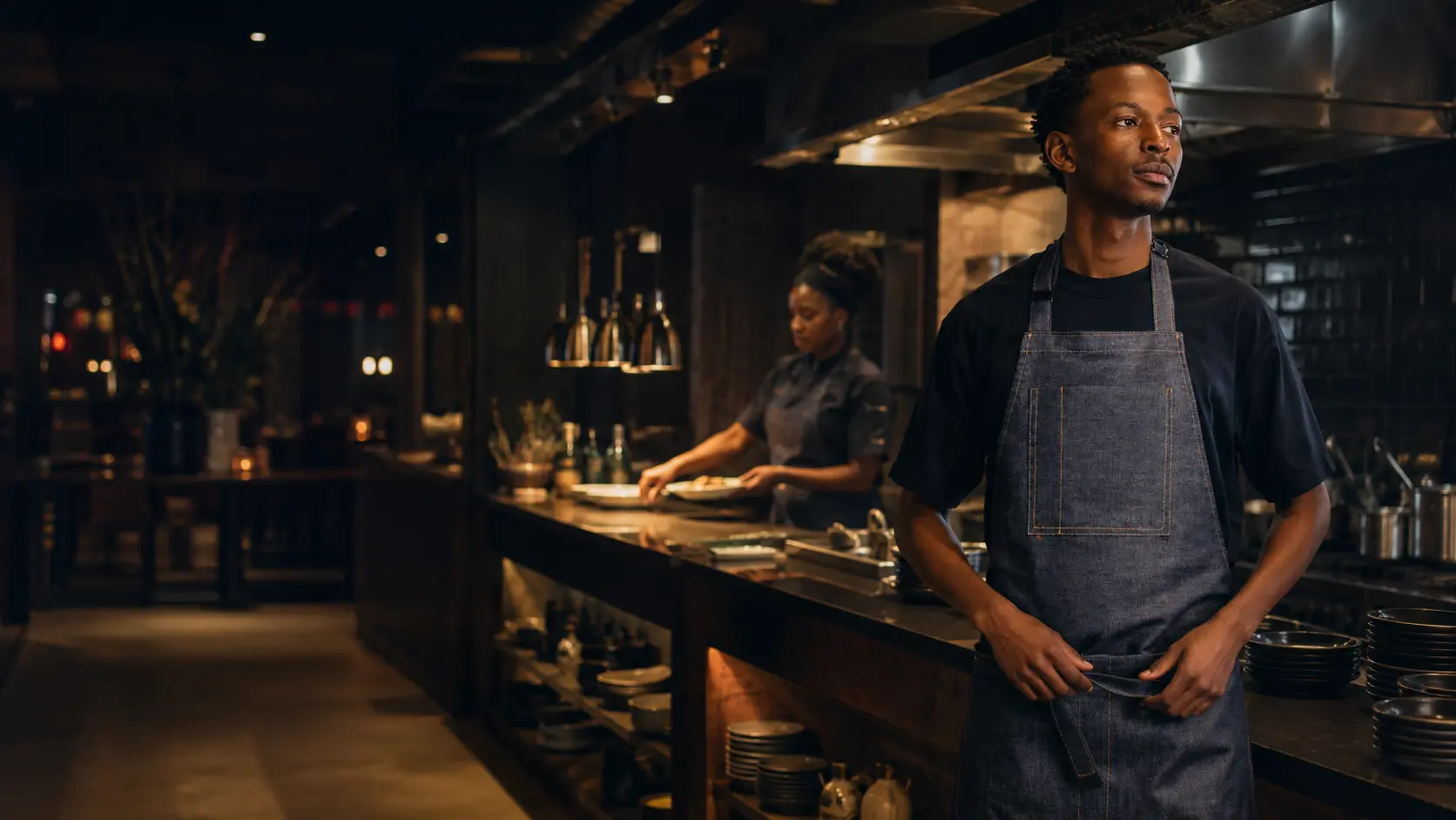 Hospitality professionals wearing dark denim aprons in a restaurant kitchen